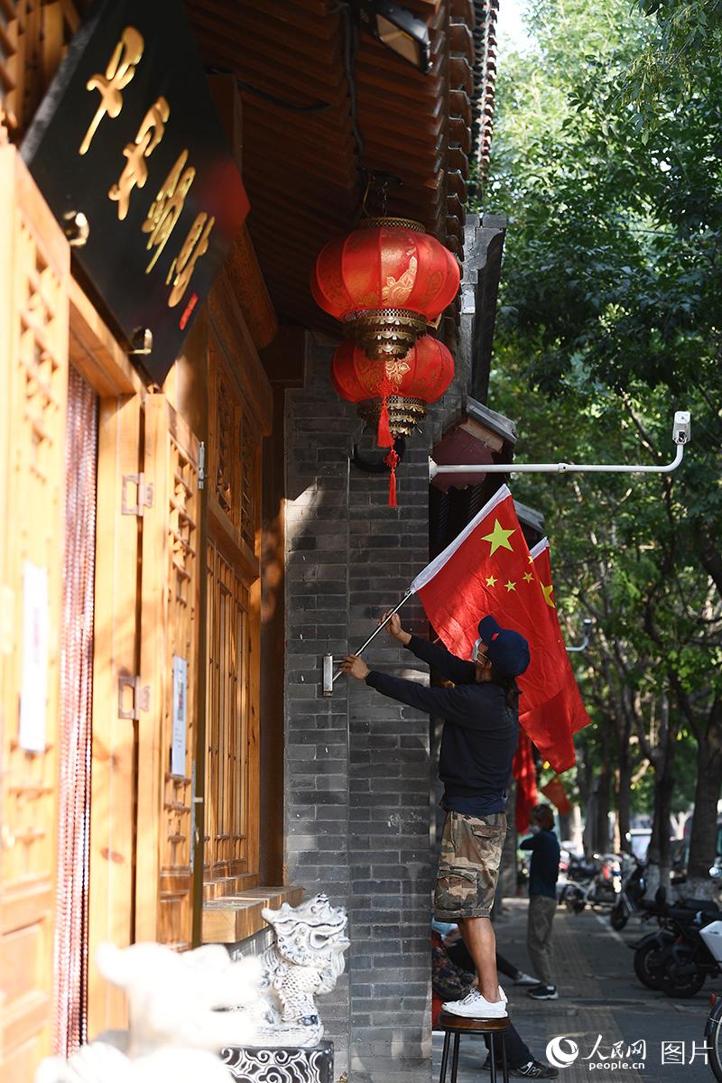 9月30日，在北京西興隆街，臨街商家工作人員正在懸掛國旗迎接國慶的到來。人民網(wǎng)記者 于凱攝