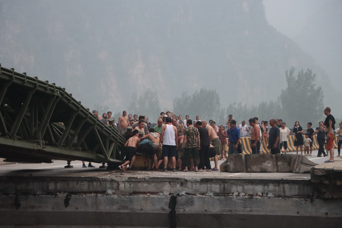 8月3日，中部戰(zhàn)區(qū)陸軍第82集團(tuán)軍某旅官兵在北京市房山區(qū)淶寶路四渡橋斷橋處架設(shè)橋梁時(shí)，當(dāng)?shù)厝罕妿椭瞥系K物。新華社發(fā)（張康 攝）