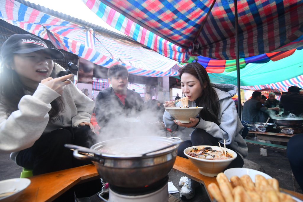 在柳州市柳江區(qū)成團(tuán)鎮(zhèn)農(nóng)貿(mào)市場(chǎng)早市，來自浙江省杭州市的游客張辰（右一）在吃早餐（11月20日攝）。新華社記者 黃孝邦 攝