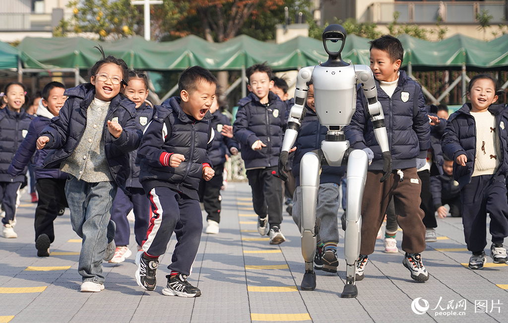 2024年12月18日，在浙江省寧波市江北區(qū)慈城懷之幼兒園，孩子們快樂的和人形機(jī)器人奔跑在校園里。人民網(wǎng) 章勇濤攝