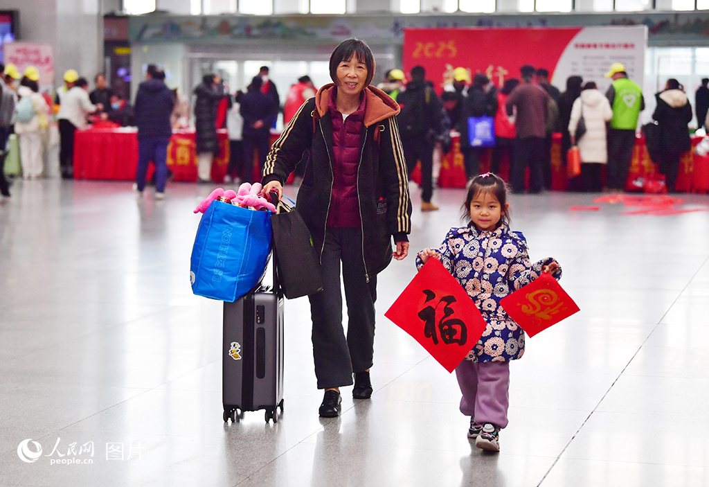 2025年春運(yùn)首日，書法家在南昌火車站候車大廳內(nèi)為乘客寫“福”字和春聯(lián)，小乘客展示領(lǐng)取到的“福”字。人民網(wǎng)記者 時雨攝