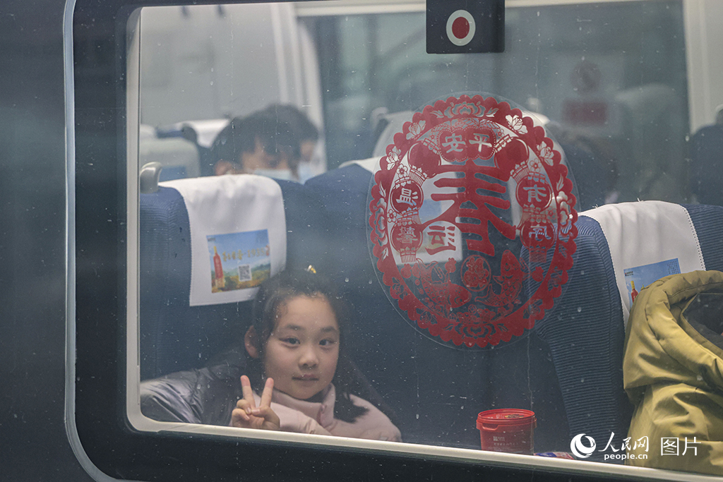 2025年春運(yùn)首日，上海虹橋火車站，一位小旅客坐在即將開行的列車上，隔著玻璃窗對鏡頭比耶。人民網(wǎng)記者 王初攝